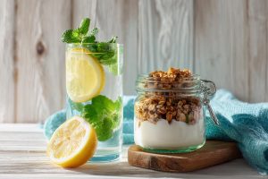 A healthy start to the day to help with constipation, featuring a tall glass of lemon water next to a bowl of Greek yogurt with fresh berries and granola.